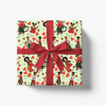 A square gift box wrapped in festive wrapping paper with a repeating pattern of Black children, red bows, and red envelopes on a pale green background, tied with a wide red ribbon and bow, shown on a clean white background.